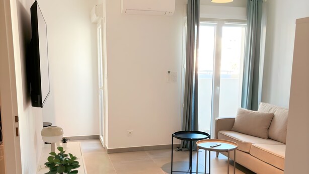 A modern living room with a sofa, a small round table, a potted plant, and a mounted TV. - Charming apartment in Ajaccio, close to the sea! (Ajaccio)