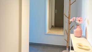 A hallway with a light fixture, a mirror, a wooden coat rack, and a table with a vase and a book. - Charming apartment in Ajaccio, close to the sea! (Ajaccio)