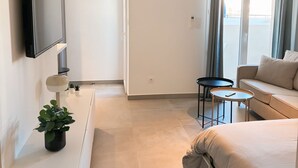 A modern hotel room with a bed, a sofa, a small table, a TV, and a potted plant. - Charming apartment in Ajaccio, close to the sea! (Ajaccio)