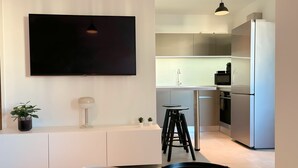 A modern living room with a flat-screen TV, a white console table, a floor lamp, and a small potted plant. - Charming apartment in Ajaccio, close to the sea! (Ajaccio)