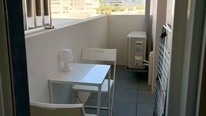 A balcony with two white tables and chairs, a small heater, and a view of buildings in the distance. - Charming apartment in Ajaccio, close to the sea! (Ajaccio)