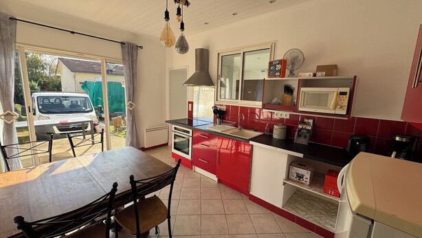 Une cuisine avec des meubles de rangement rouges et blancs, un four à micro-ondes, un évier et une table à manger avec des chaises.