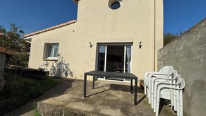 Une maison dotée d’un patio comprenant une table et des chaises, une porte-fenêtre coulissante et une petite fenêtre.