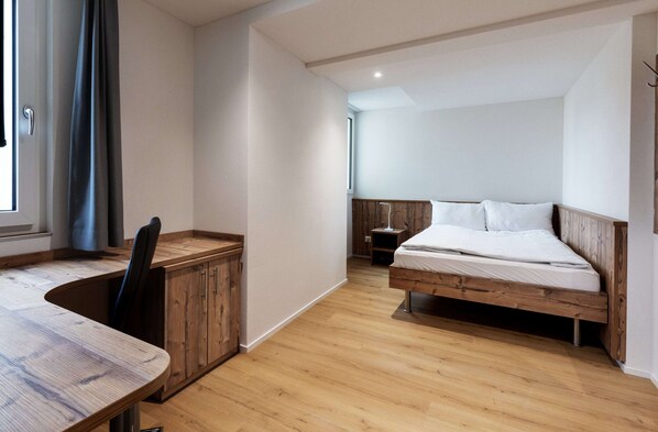 A bedroom with a wooden bed, a desk, and a chair. - Hotel MeiSTAY - Self-Check-in (Meisterschwanden)