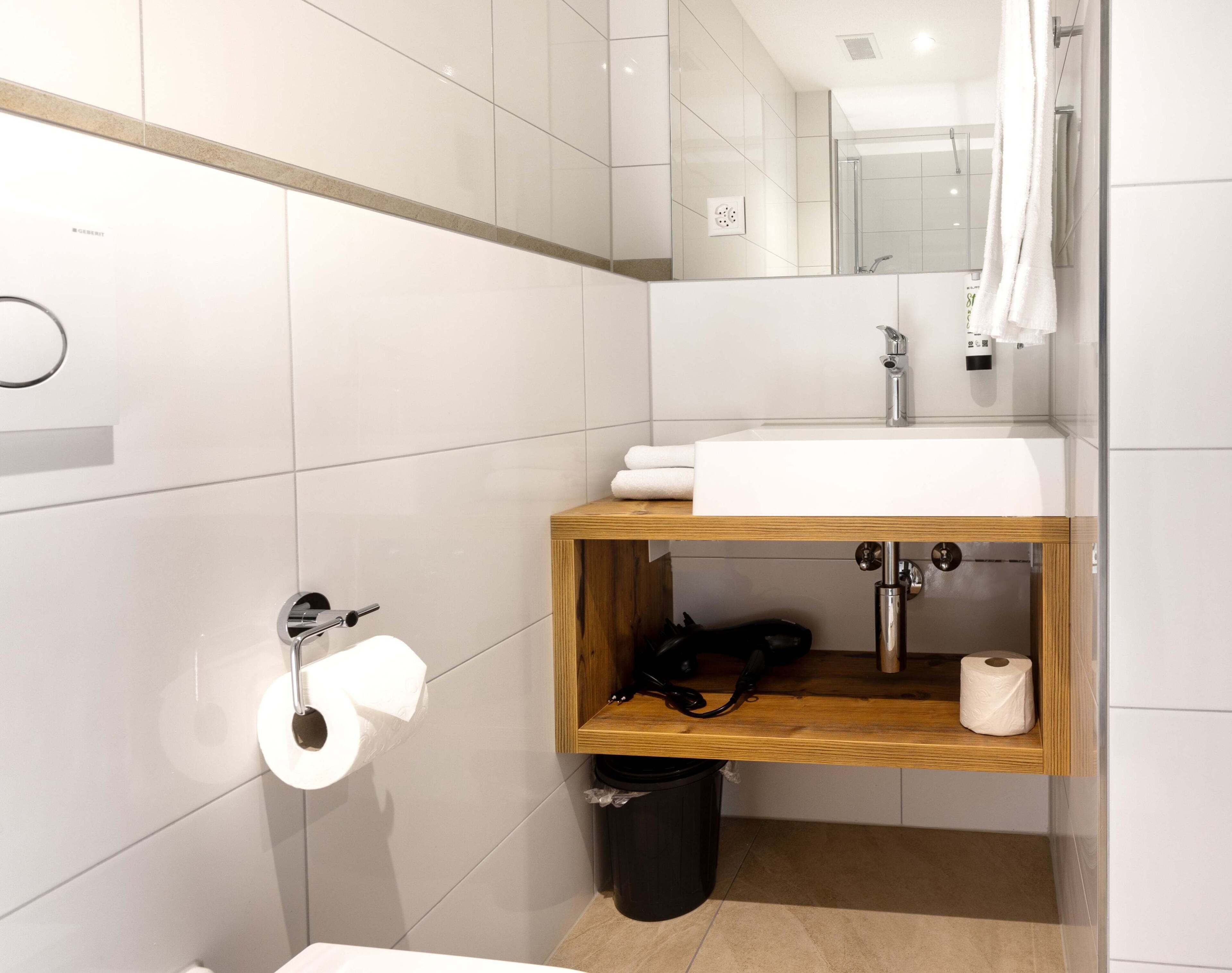 Een moderne badkamer met een witte wastafel, een houten opbergmeubel en een douchecabine met glazen wanden.