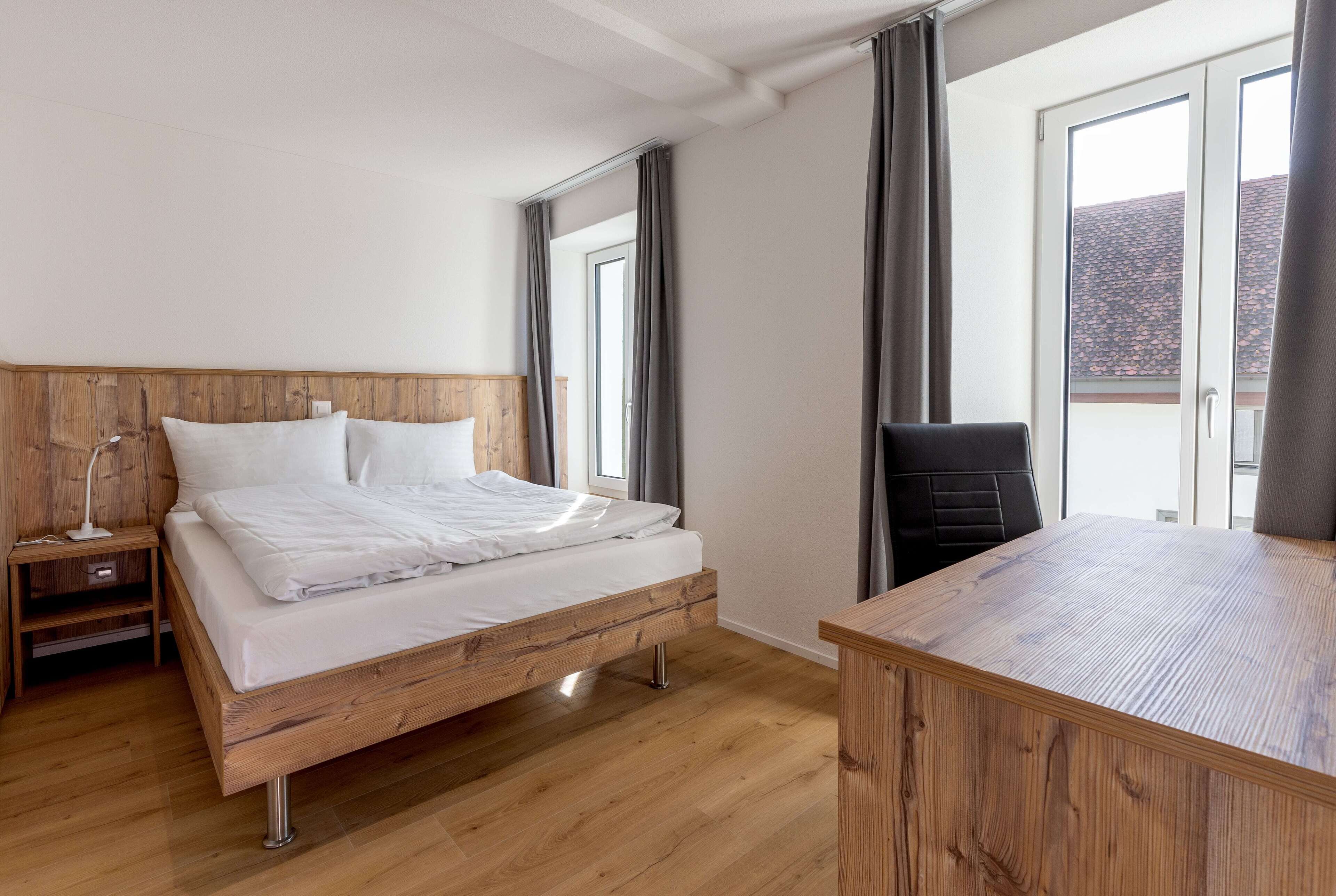 A bedroom with a wooden bed, a nightstand, a desk, and a chair.
