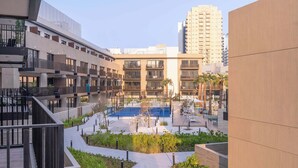 A modern urban residential area with a central courtyard featuring a swimming pool, surrounded by multi-story buildings with balconies and a tall building in the background.