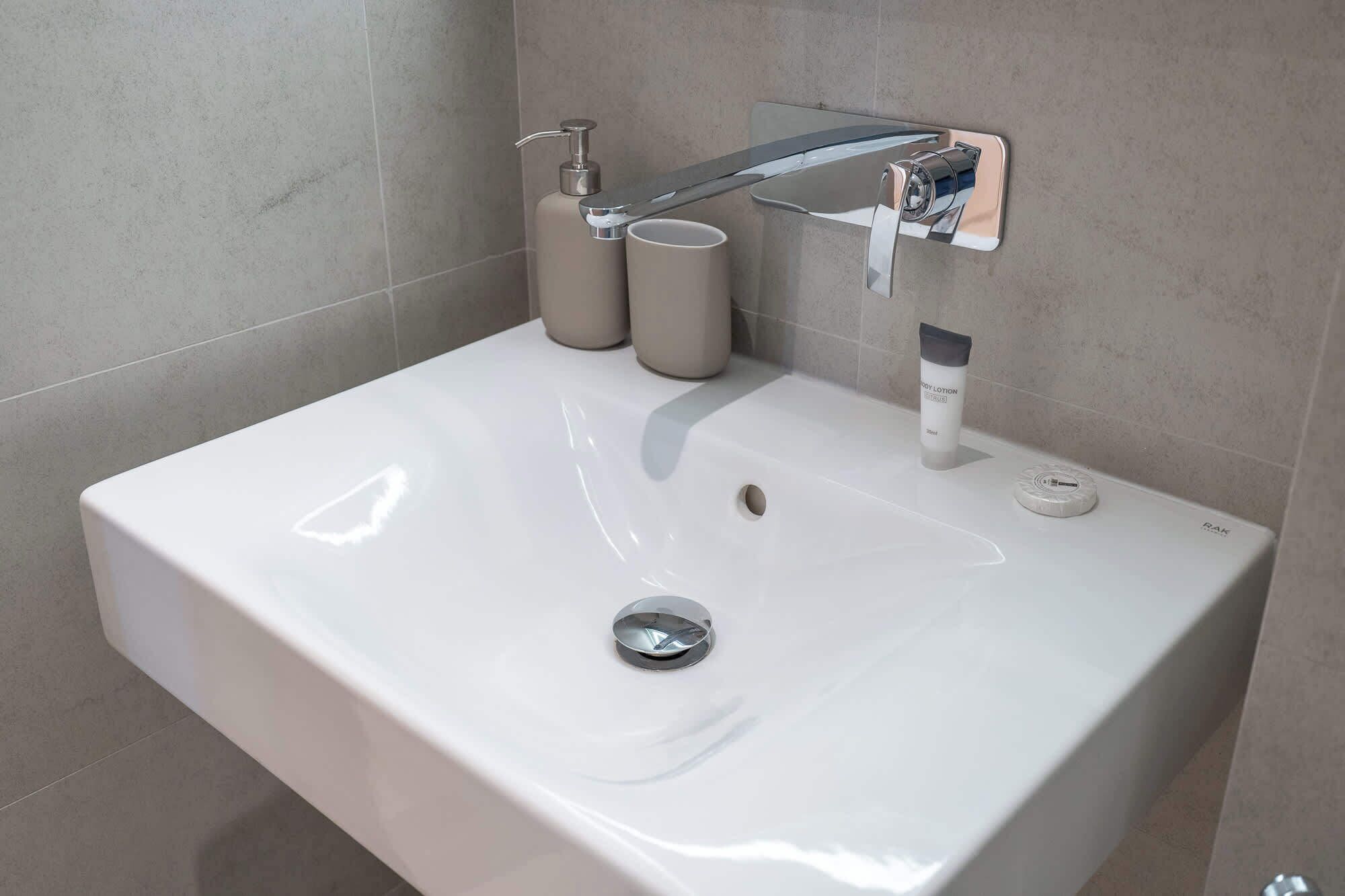 A modern bathroom sink with a chrome faucet, two soap dispensers, and a bottle of body lotion.