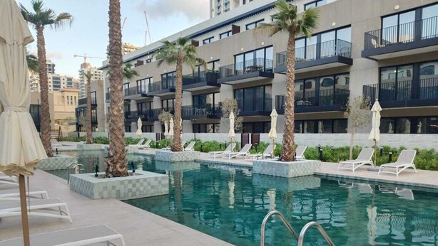 A swimming pool with lounge chairs and palm trees, surrounded by a modern building with balconies.