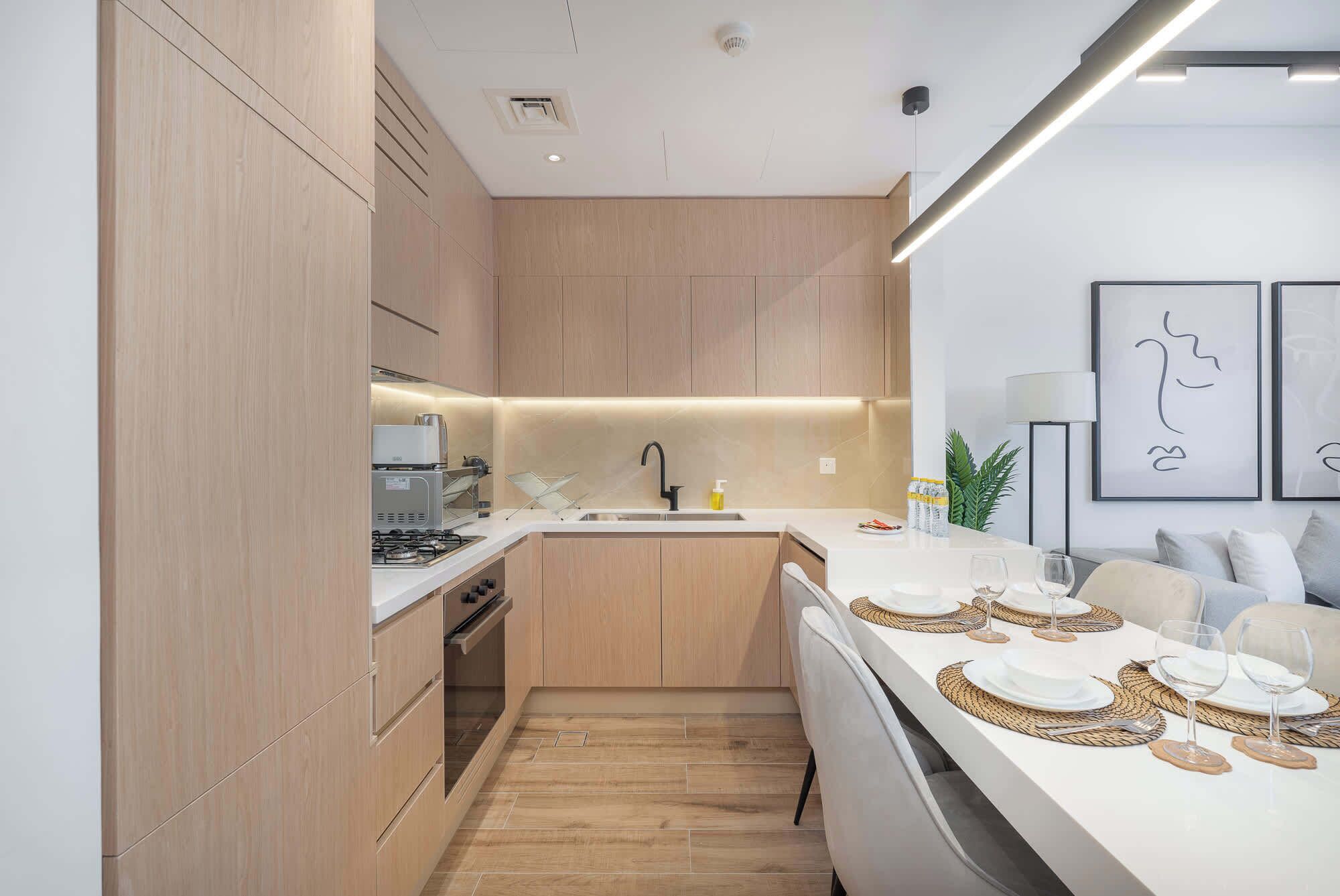 Una cocina moderna con armarios de madera, horno integrado y comedor con una mesa blanca preparada para cuatro.