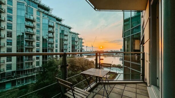A balcony with a view of a river and sunset, featuring a table and chairs. - Londonaprt/sleeps6/gym/waterfront/wifi (London)