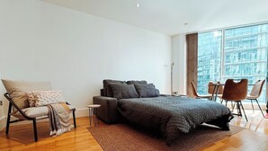 A modern bedroom with a large bed, a sofa, a chair, and a dining table. - Londonaprt/sleeps6/gym/waterfront/wifi (London)