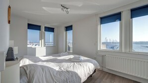 A hotel room with a large bed, two windows with views of a marina, a radiator, and a ceiling light fixture. - Summio Marina Port Zélande (Ouddorp)