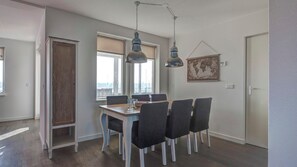 A dining area with a wooden table and chairs, large windows, and hanging pendant lights. - Summio Marina Port Zélande (Ouddorp)
