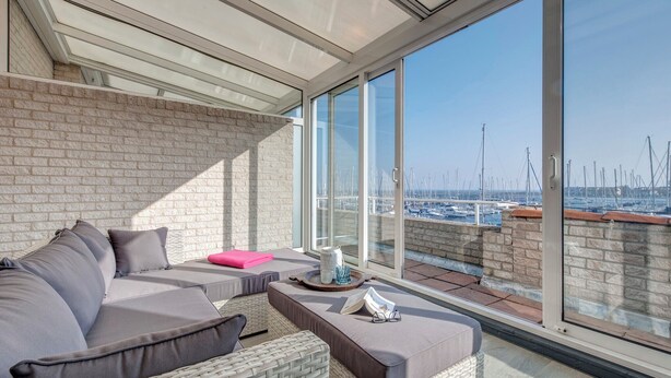 A balcony with a view of a marina, featuring a sofa, cushions, and a tray with a cup and a decorative item. - Summio Marina Port Zélande (Ouddorp)