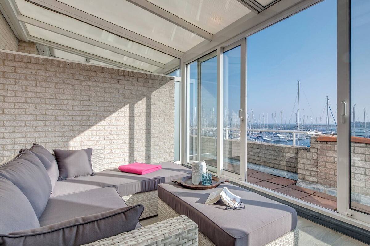 A balcony with a view of a marina, featuring a sofa, cushions, and a tray with a cup and a decorative item.