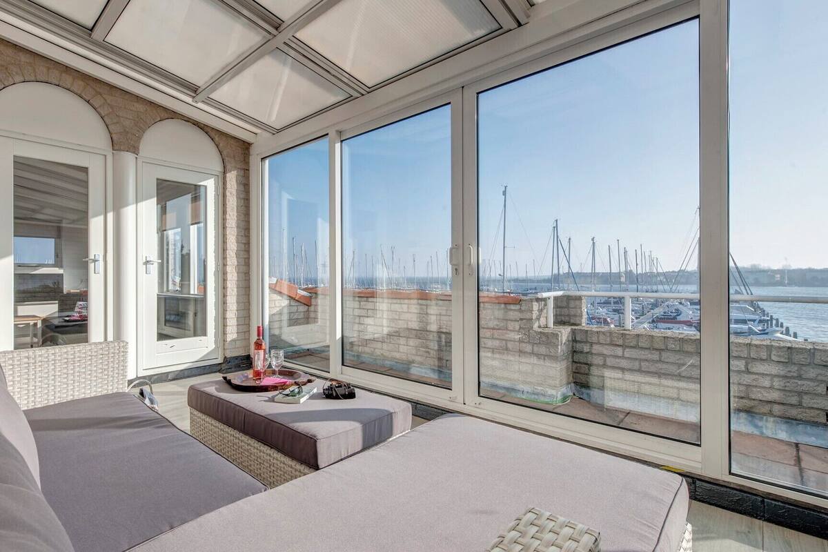 A balcony with a view of a marina, a cushioned seating area, and a glass door leading to an interior space.