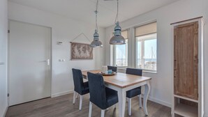 A dining area with a wooden table and four chairs, two pendant lights, a window with a view of a marina, and a wooden wardrobe. - Summio Marina Port Zélande (Ouddorp)