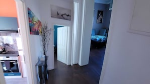 Un pasillo con una puerta que da a un dormitorio, una pequeña mesa con un florero, y un cuadro en la pared.