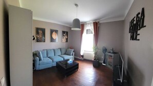 Una sala de estar con un sofá azul claro, una mesa de centro negra, una lámpara de techo y un radiador.