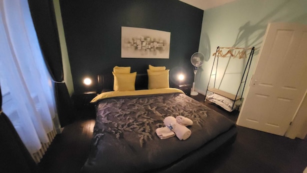 Un dormitorio con cama, una obra de arte en la pared, una mesita de noche con lámpara, un sillón colgante y una puerta.