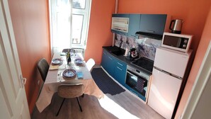 Cocina compacta con mesa, sillas, microondas, horno y ventana con cortinas.