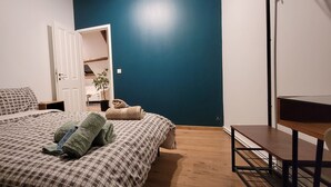 Un dormitorio con cama, escritorio y silla. Se ve una puerta que da a otra habitación.