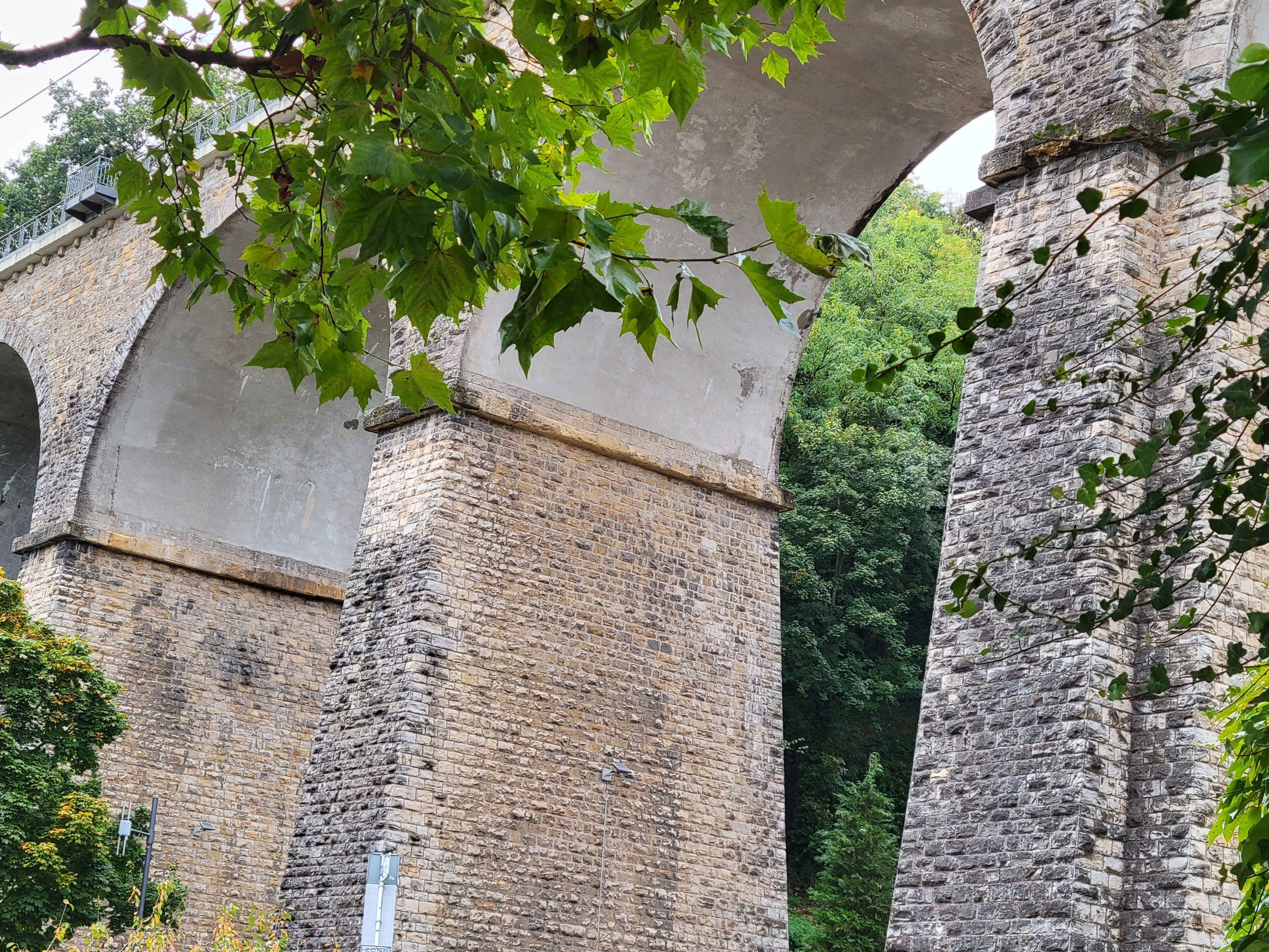Un pont en pierre doté d’une rambarde métallique, entouré de verdure.