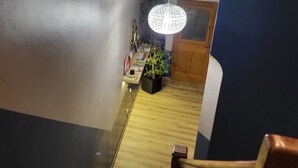 Un pasillo con suelo de madera, un escritorio con una planta y una puerta al fondo.