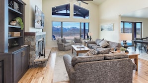 A spacious living room with a fireplace, large windows offering mountain views, and a dining area with a view. - New Custom Home on 35 Acres - Amazing Mtn Views -15 Min to DGO - AC/Hot Tub (Durango)