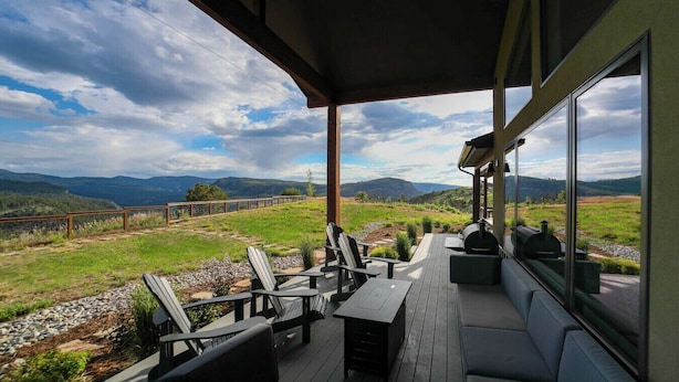 A covered outdoor seating area with chairs and a table, overlooking a scenic landscape with mountains and a lake. - New Custom Home on 35 Acres - Amazing Mtn Views -15 Min to DGO - AC/Hot Tub (Durango)