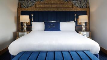 Una cama grande con cabecera azul, ropa de cama blanca y un banco azul a juego al pie de la cama.