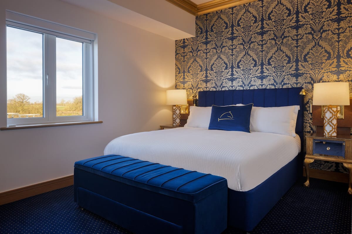 A bedroom with a large bed, a window, and patterned wallpaper.