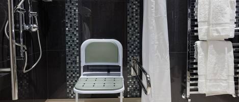 A modern bathroom with a shower, a white chair, a towel rack, and a tiled wall.