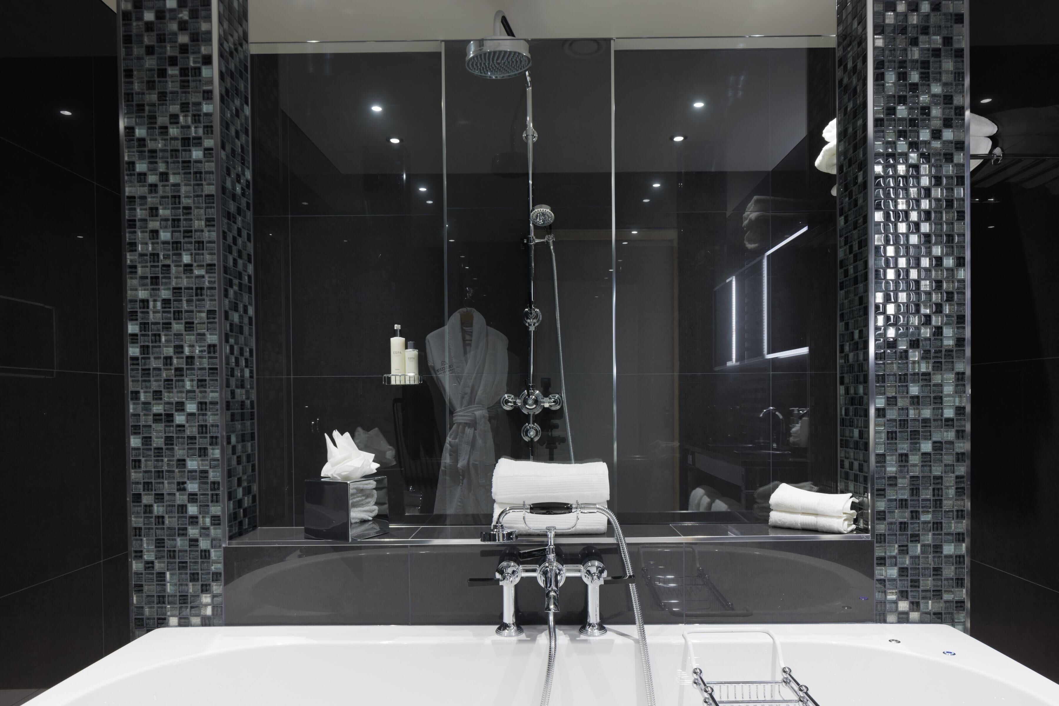 A modern bathroom with a large bathtub, a glass-enclosed shower area, and a mirror reflecting the room.