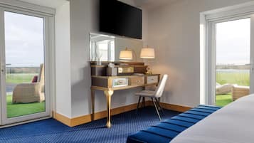 Habitación de hotel con una cama grande, un escritorio con una silla, un televisor sobre el escritorio y vistas al exterior a través de las ventanas.