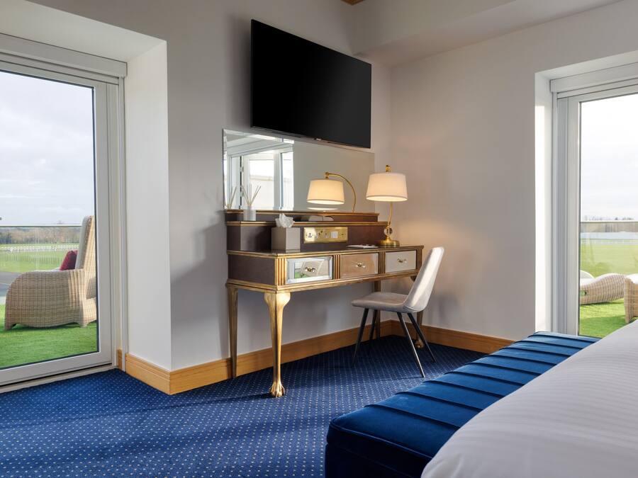 Habitación de hotel con una cama grande, un escritorio con una silla, un televisor sobre el escritorio y vistas al exterior a través de las ventanas.