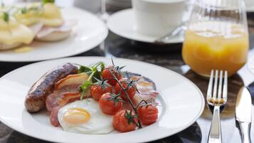 Un plato de desayuno con huevos, tocino, salchichas y tomates sobre un plato blanco.