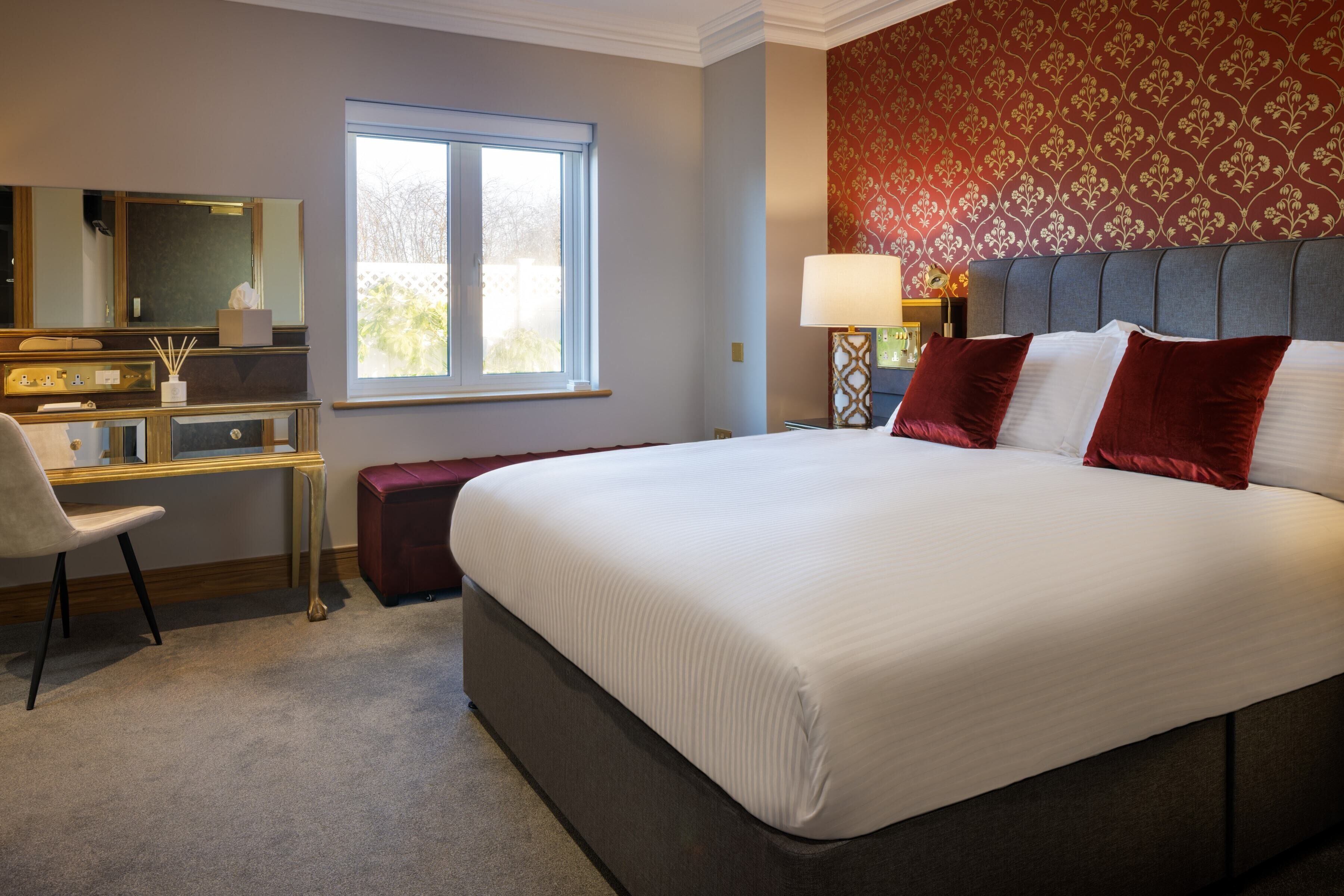 Ein Hotelzimmer mit einem großen Bett, einem Schreibtisch, einem Stuhl, einem Fenster und einer Wand mit Muster.