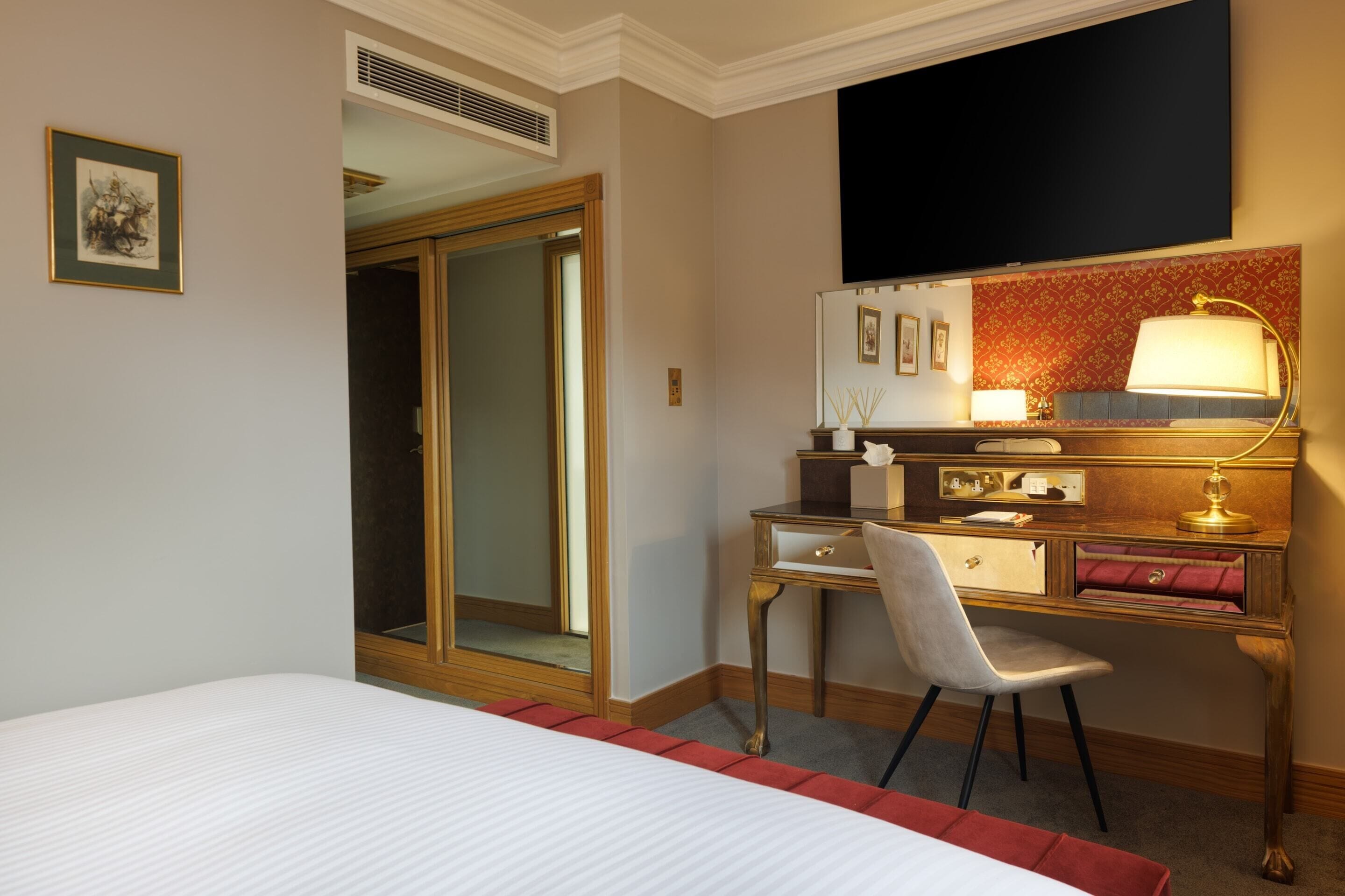A hotel room with a bed, a desk with a chair, a television, and a wardrobe.