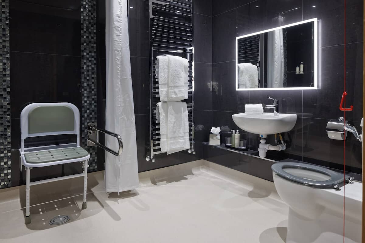 A modern bathroom with a white sink, a toilet, a shower area, and a wheelchair-accessible bench.