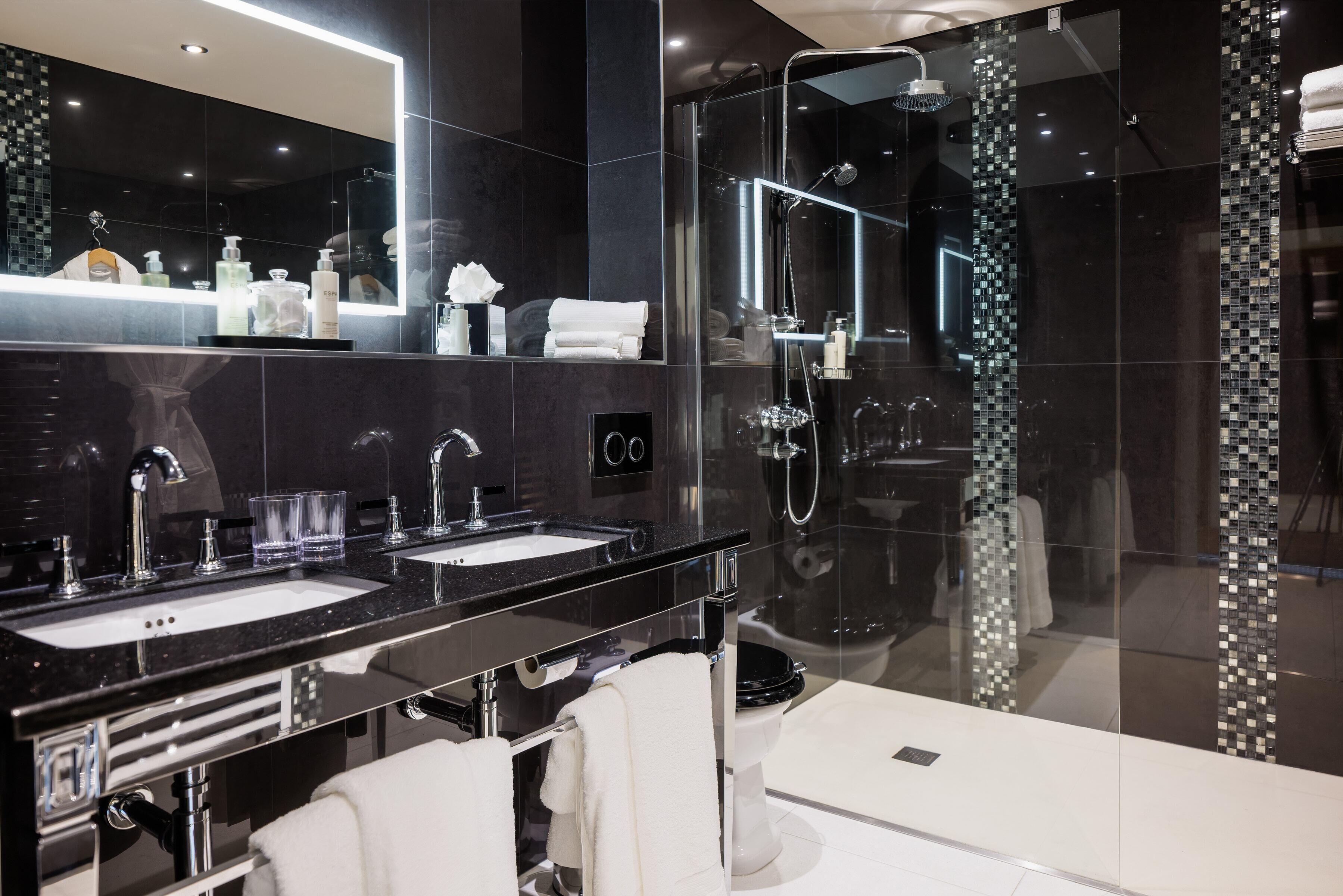 A modern bathroom with two sinks, a large mirror, and a glass-enclosed shower area.