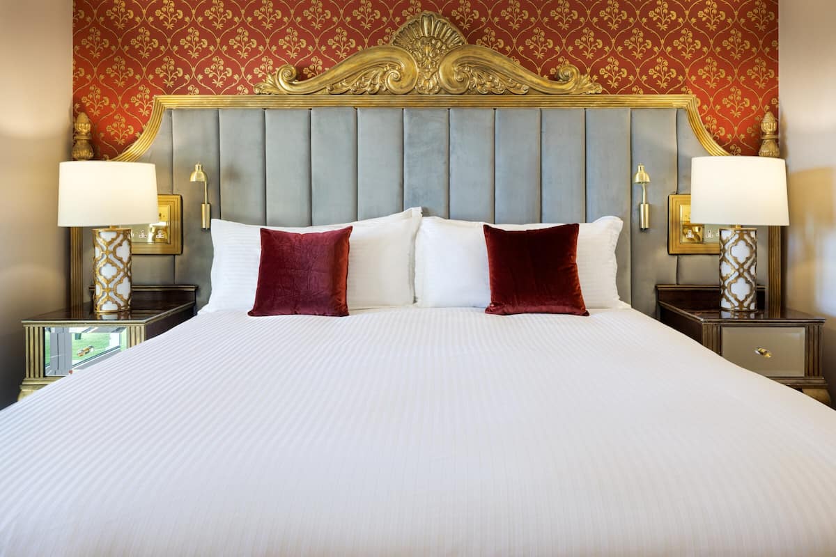 A large bed with a grey upholstered headboard, two white pillows, and two red pillows. There are two bedside tables with lamps and framed pictures.