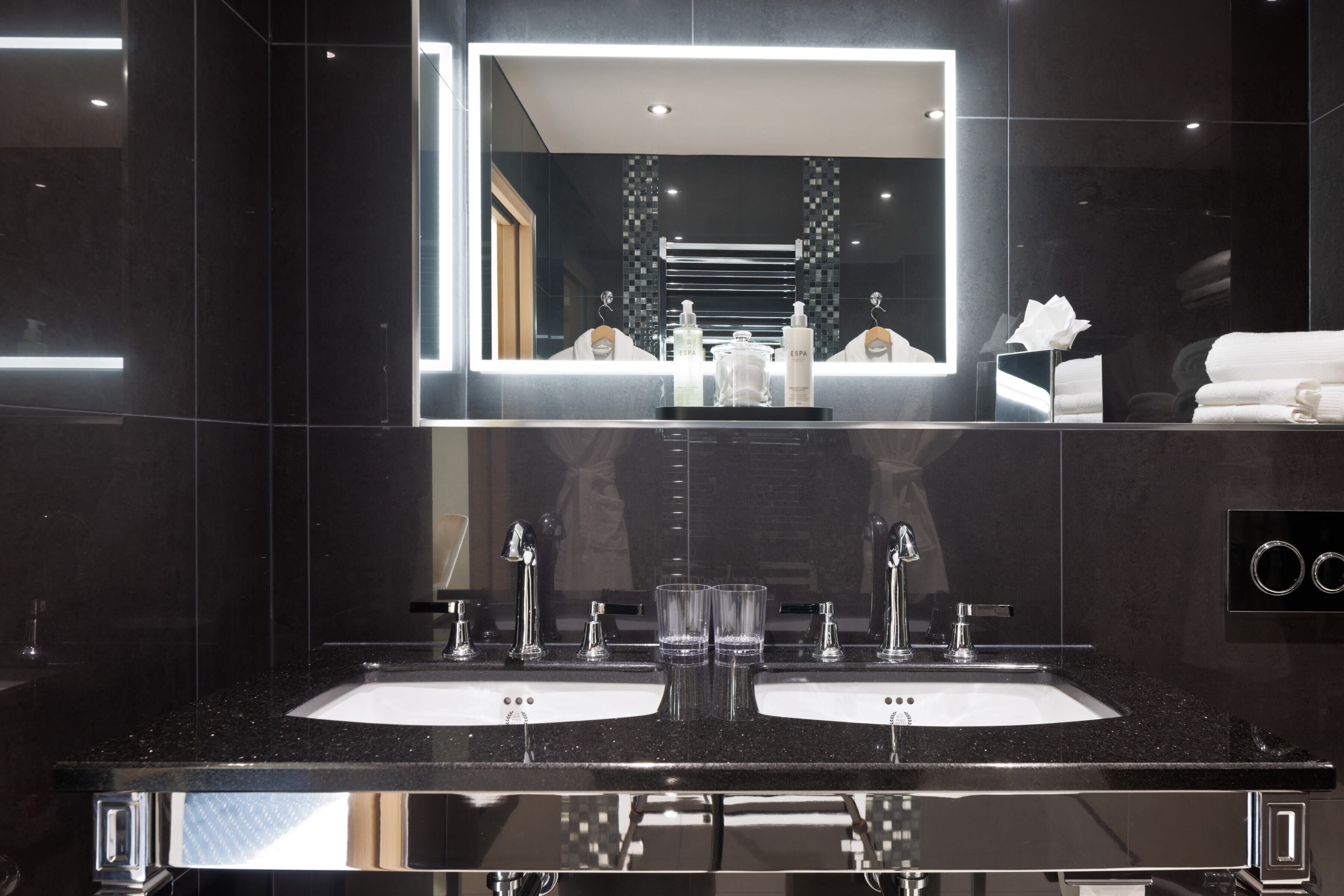 Un baño moderno con dos lavamanos, un espejo grande y un perchero para toallas.