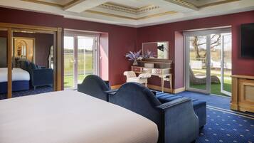 A hotel room with a large bed, a seating area with blue upholstered chairs, a small table, and a large window offering a view of the outdoors.