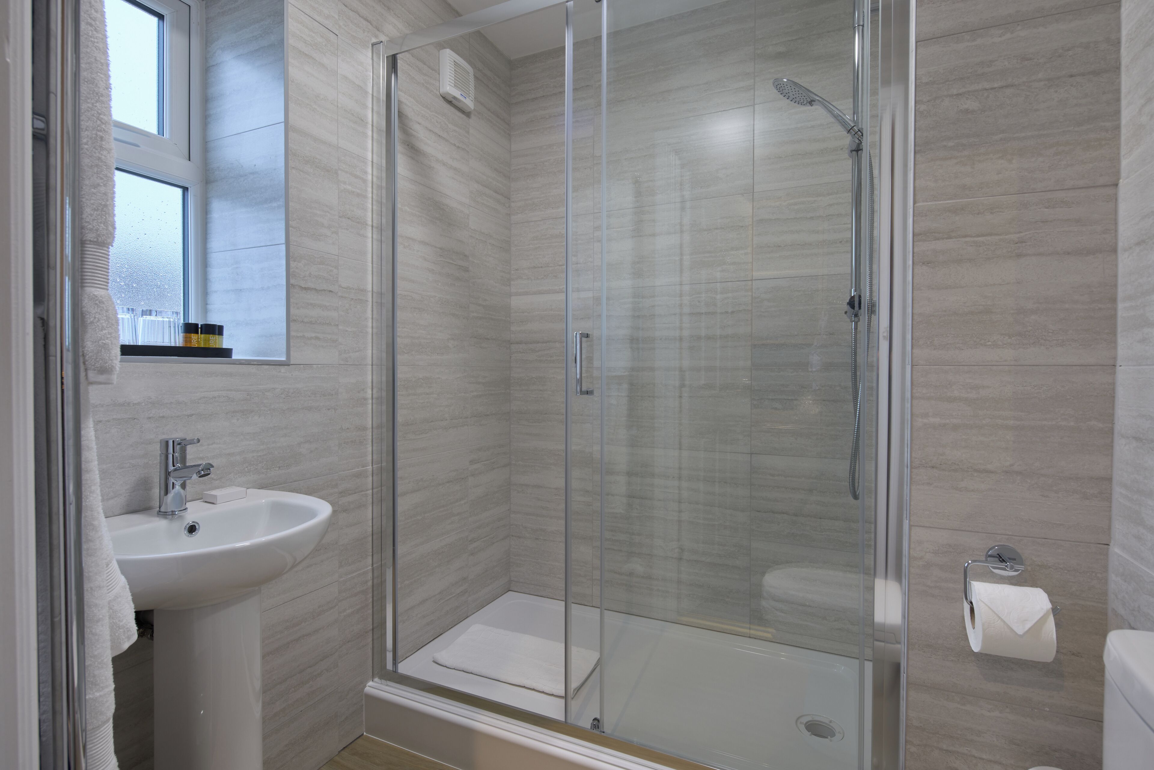 A modern bathroom with a glass-enclosed shower, a white sink, and a toilet.