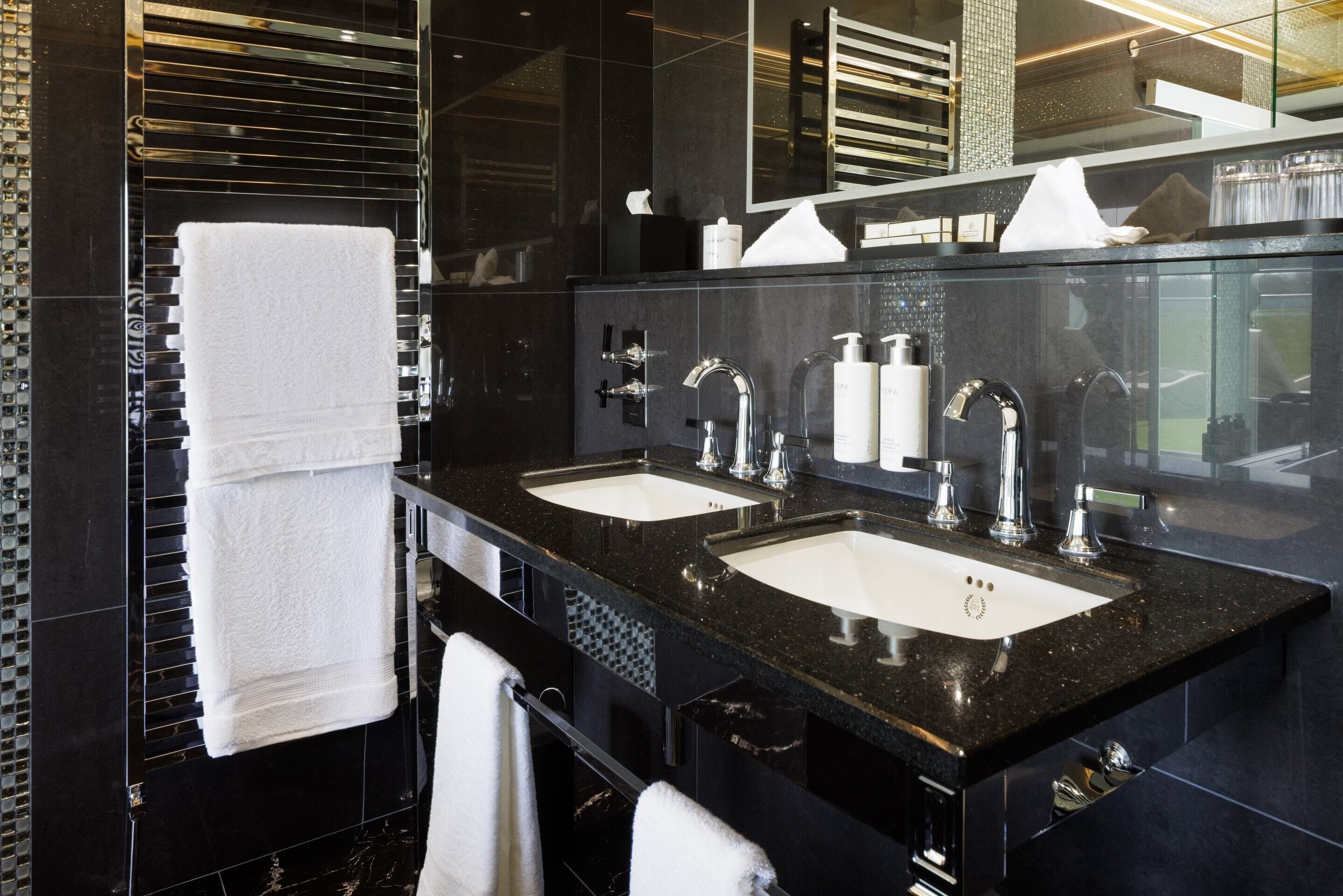 A modern bathroom with two sinks, a large mirror, and a towel rack.
