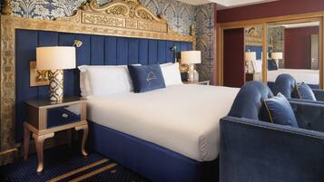 A hotel room with a large bed, two bedside tables with lamps, a mirror, and a blue upholstered chair.