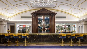 Eine Bar mit Marmorplatte, goldenen Akzenten und blauen Barhocker.