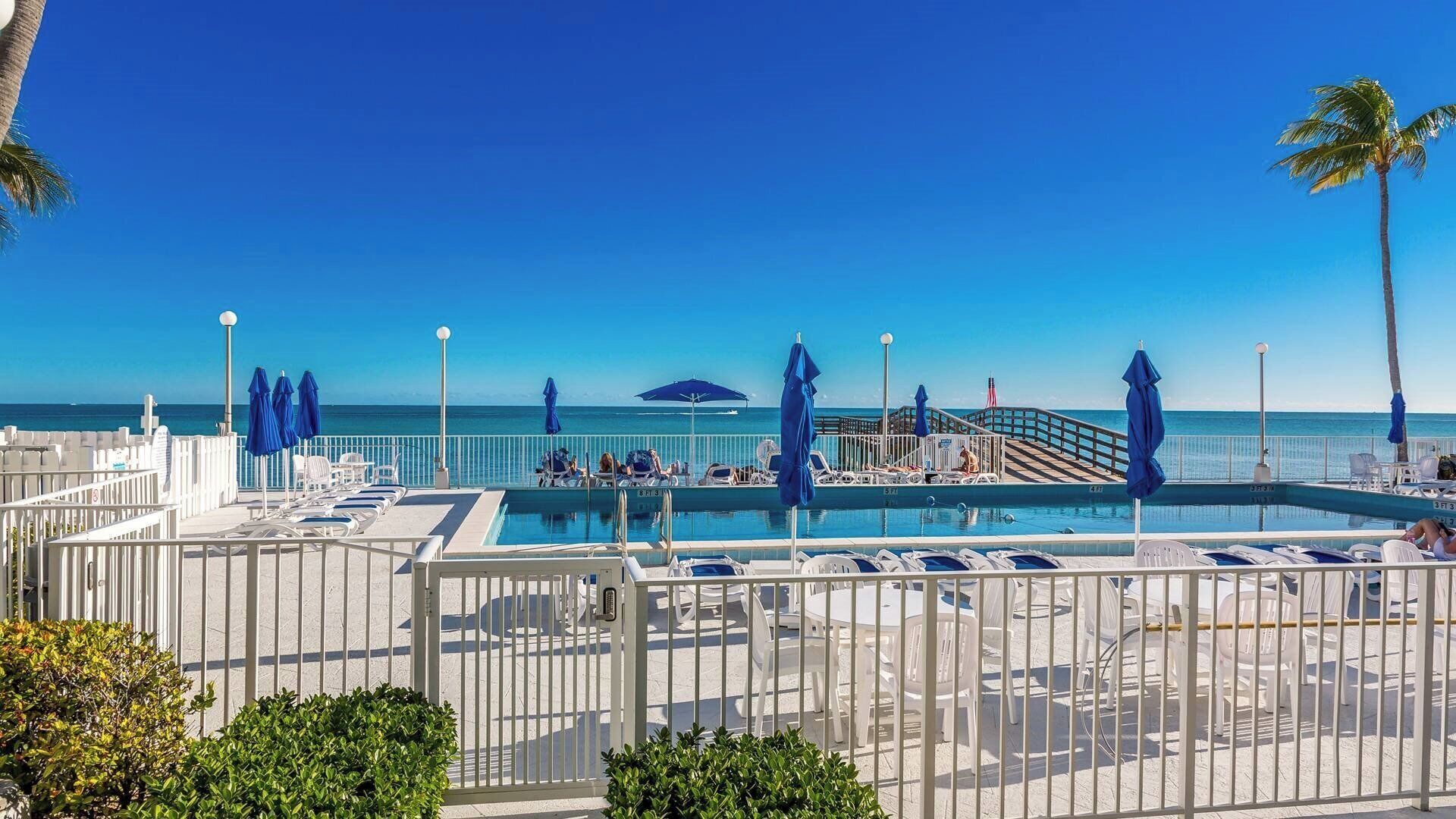 A pool area with lounge chairs, umbrellas, and a view of the ocean.